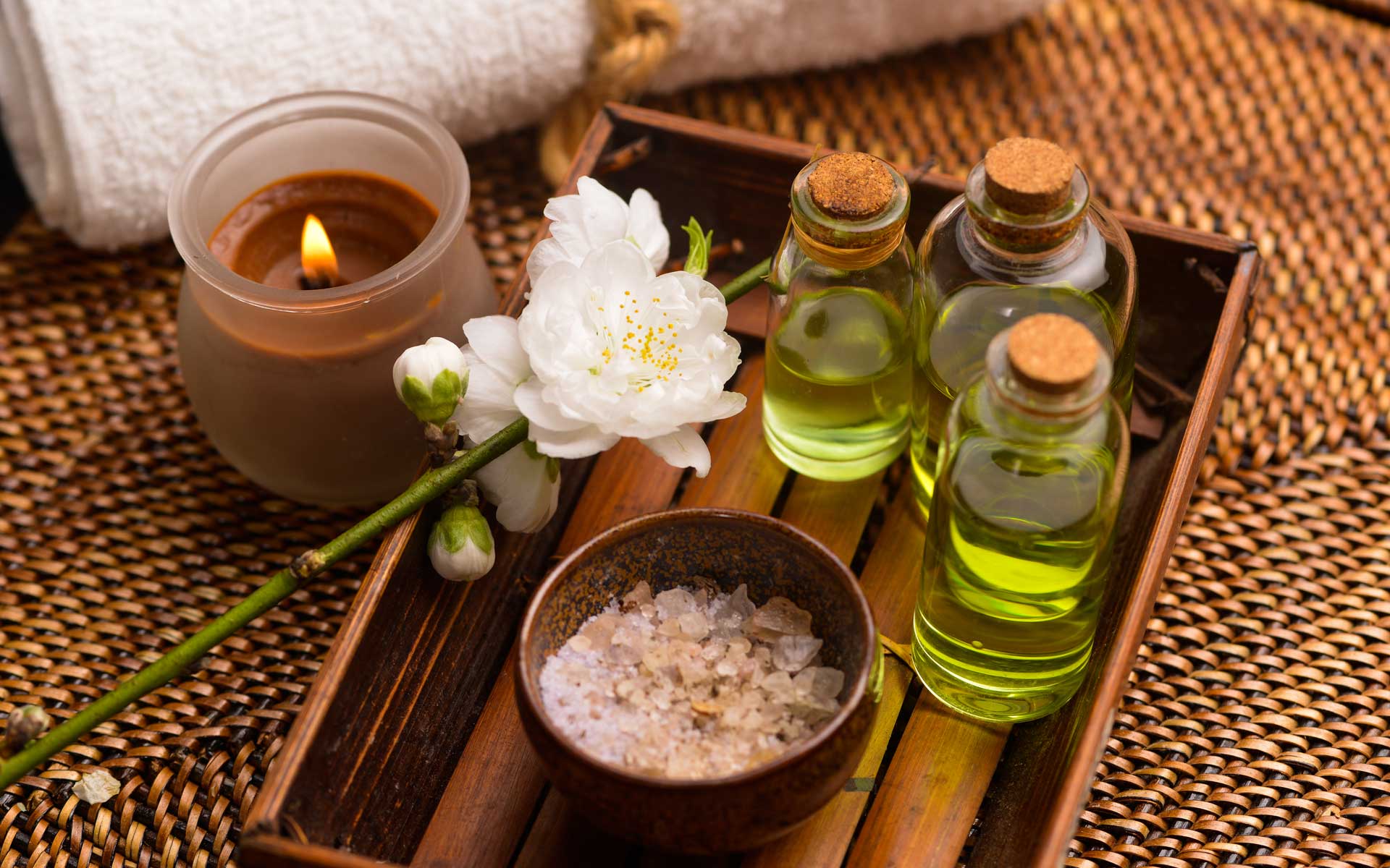 Spa tray and lit candle with rolled towel, salt bowl, and oil jars